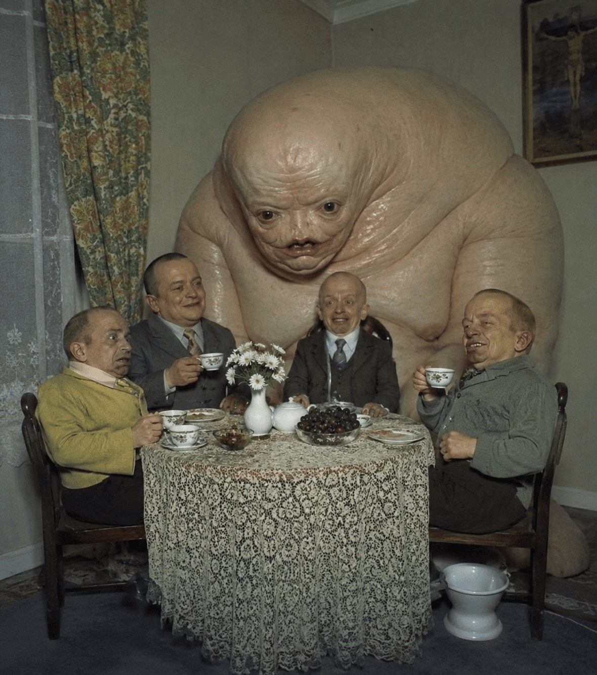Four men have tea beside a large creature prop.