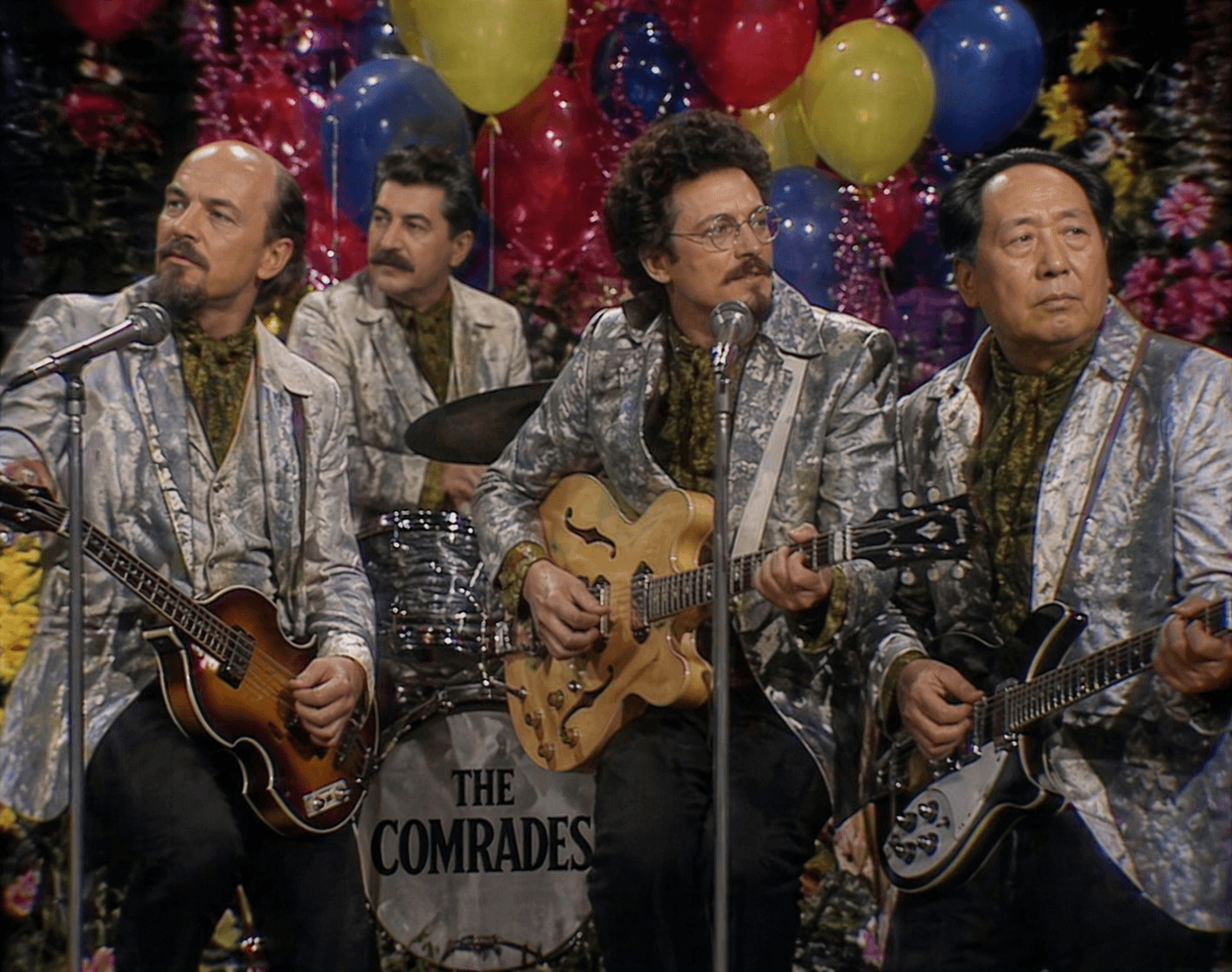 Four musicians in matching jackets perform as The Comrades.